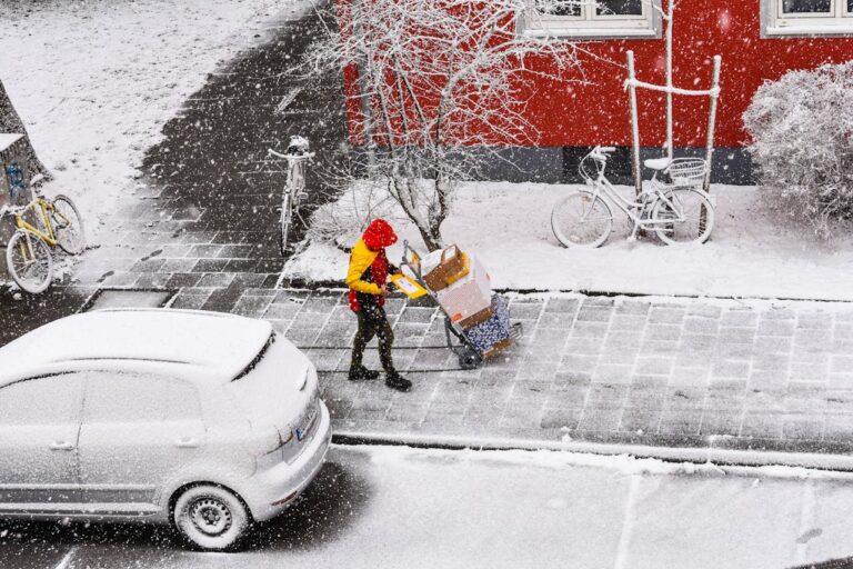 Man in Red Jacket and Black Pants Walking on Snow Covered Road